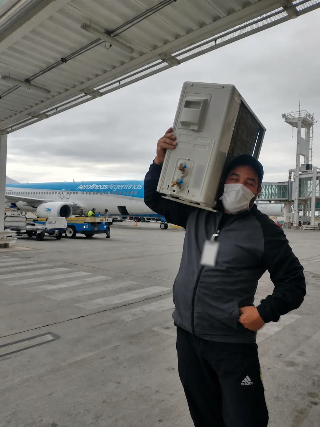Técnico sosteniendo un equipo de climatización delante de una aeronave en un aeropuerto.
