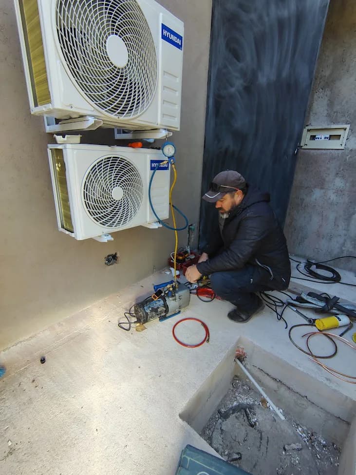 Técnico trabajando junto a dos unidades exteriores de aire acondicionado y herramientas de medición.
