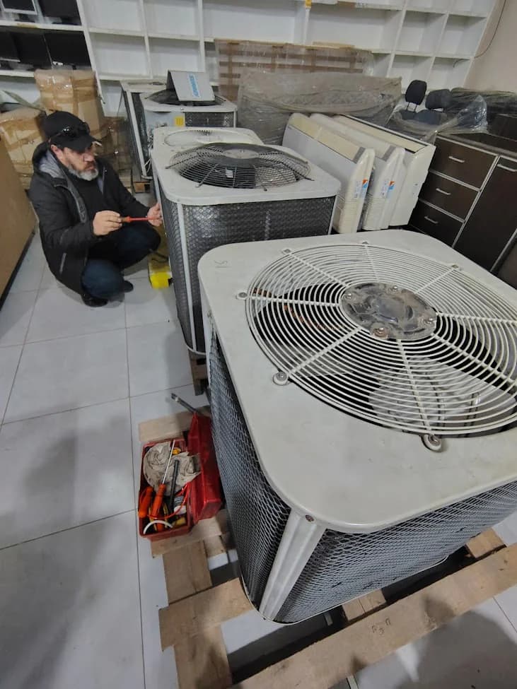 Técnico agachado junto a varias unidades exteriores de climatización y una caja de herramientas.